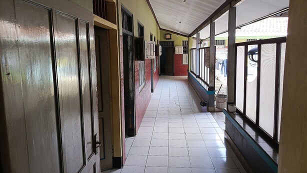 A corridor with tiled flooring, metal doors, and windows with blinds. - Hotel O Dian Asih Rooms (Demak)