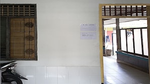 A hallway with a tiled floor, a window with a decorative grille, and a sign on the wall. - Hotel O Dian Asih Rooms (Demak)