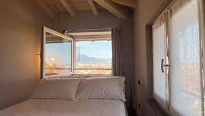 A bedroom with a bed, a window with curtains, and a view of a cityscape.