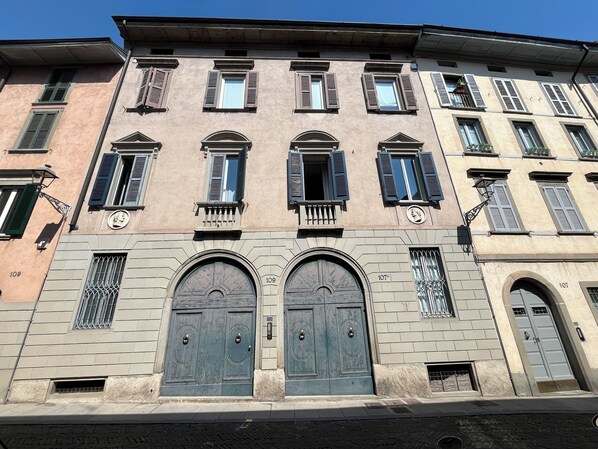 A building with multiple windows, a central entrance with two large doors, and a balcony with railings.