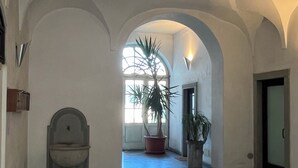 A spacious hallway with arched ceilings and a large window allowing natural light. A toilet is visible on the left, and a potted plant is in the center.