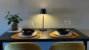 A dining table with two black bowls, a fork, a knife, and two wine glasses. A black lamp is on the table, and a plant is in the background.