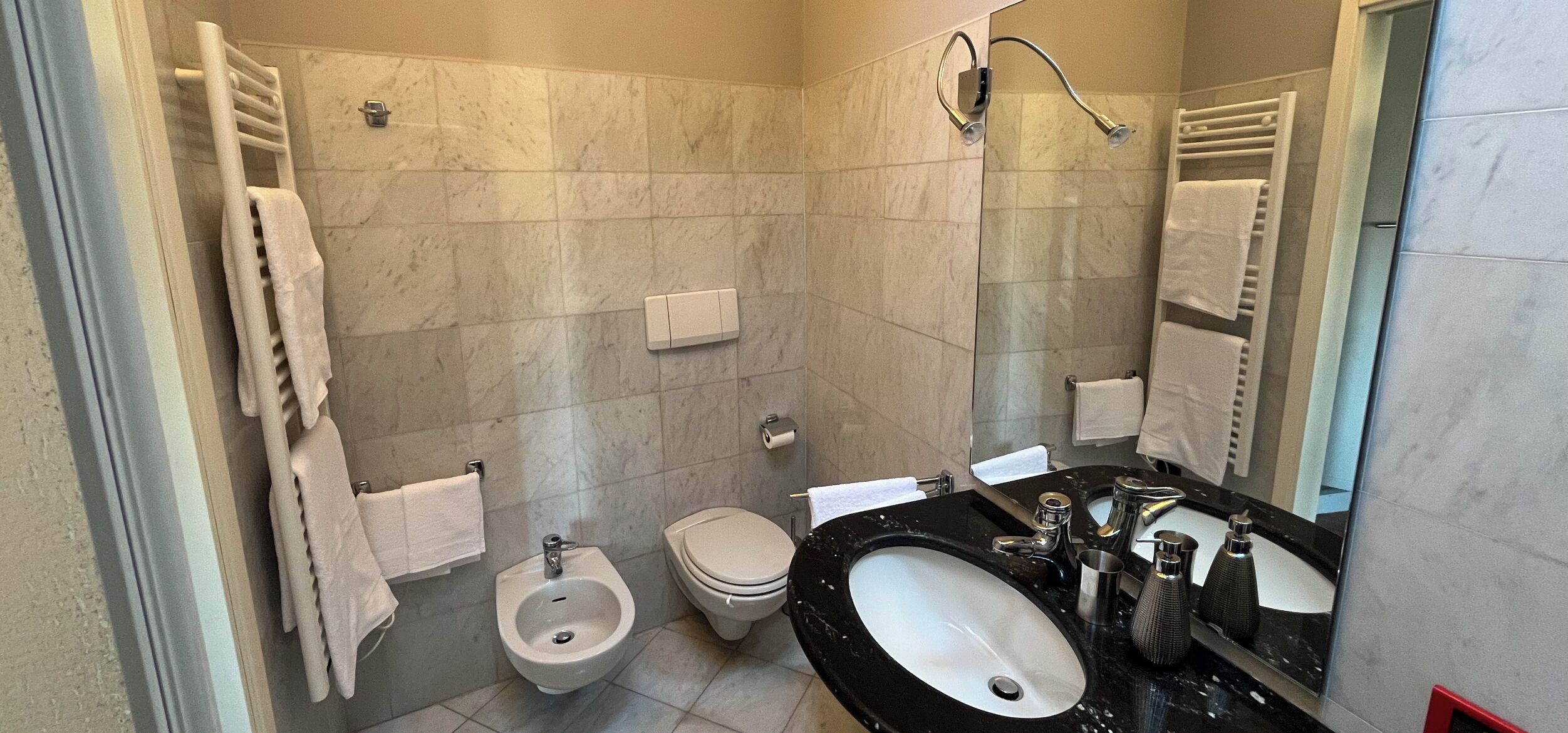 Ein modernes Badezimmer mit einer Bidet, Toilette und einem großen Waschbecken mit Spiegel.