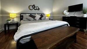 Een moderne slaapkamer met een bed, nachtkastjes, een bankje, een televisie en een kunstwerk aan de muur.
