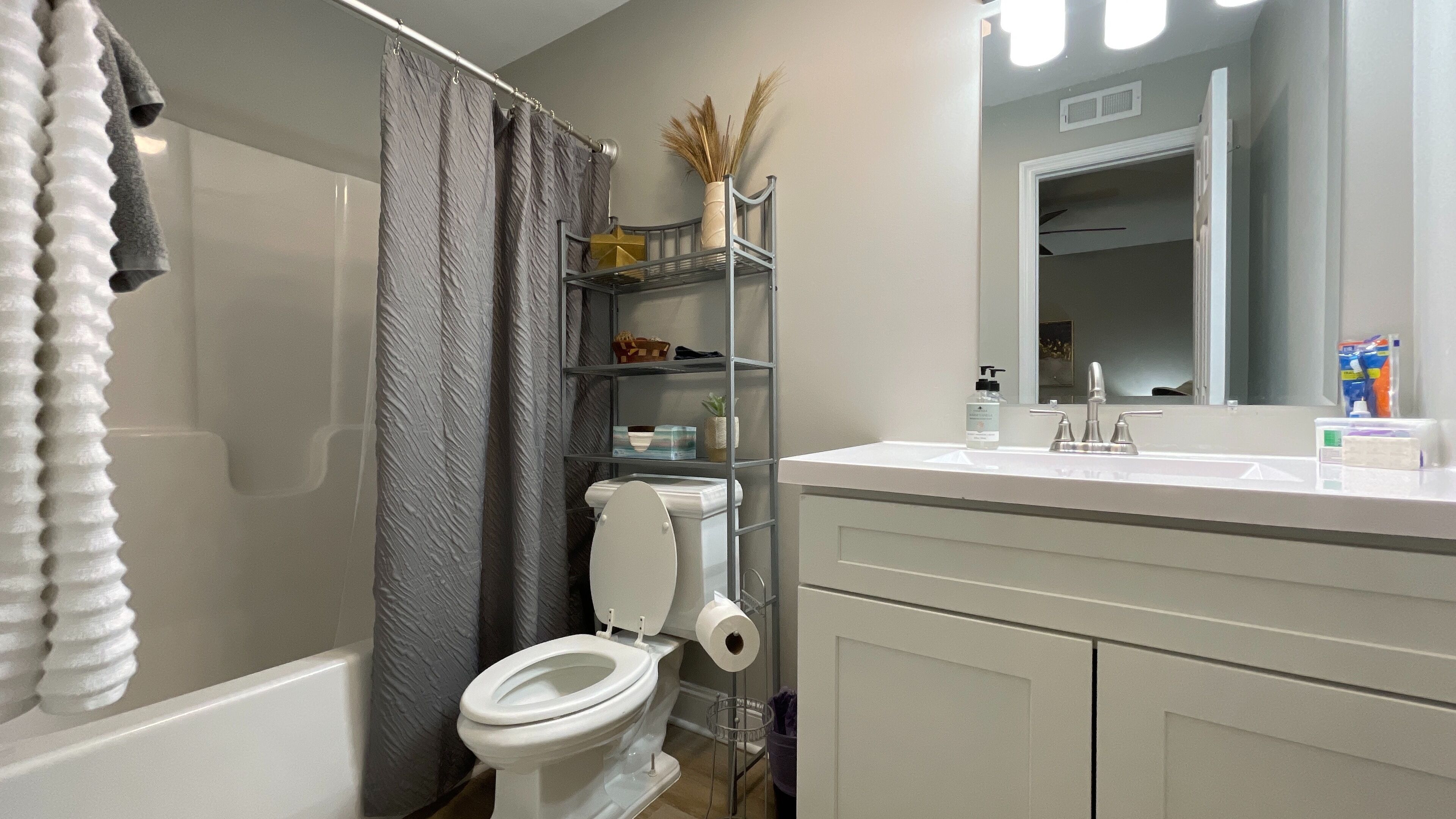 Ein modernes Badezimmer mit Toilette, Duschvorhang, Waschtisch mit Spiegel und Ablageflächen für Toilettenartikel.