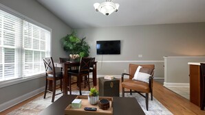 A living room with a dining area, a flat-screen TV mounted on the wall, and a ceiling fan. - Elegant 2BR | Modern Amenities & Convenient Flair (Johnson City)