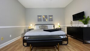 A modern bedroom with a bed, bedside lamps, a TV, and decorative wall art. - Elegant 2BR | Modern Amenities & Convenient Flair (Johnson City)