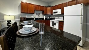Una cocina moderna con armarios de madera, un refrigerador blanco, un microondas y una estufa. Hay una mesa de comedor con sillas y un vaso de agua.