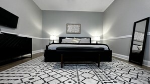 Un dormitorio con una cama, dos lámparas de noche, un televisor montado en la pared, un espejo y una alfombra estampada.