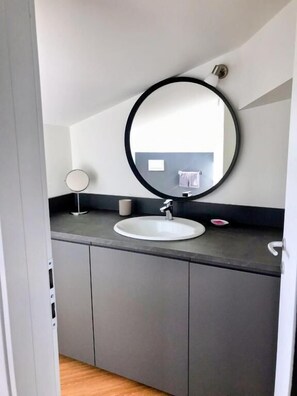 A modern bathroom with a round mirror, a white sink, and a small round table with a cup. - Monza Apartments (Monza)