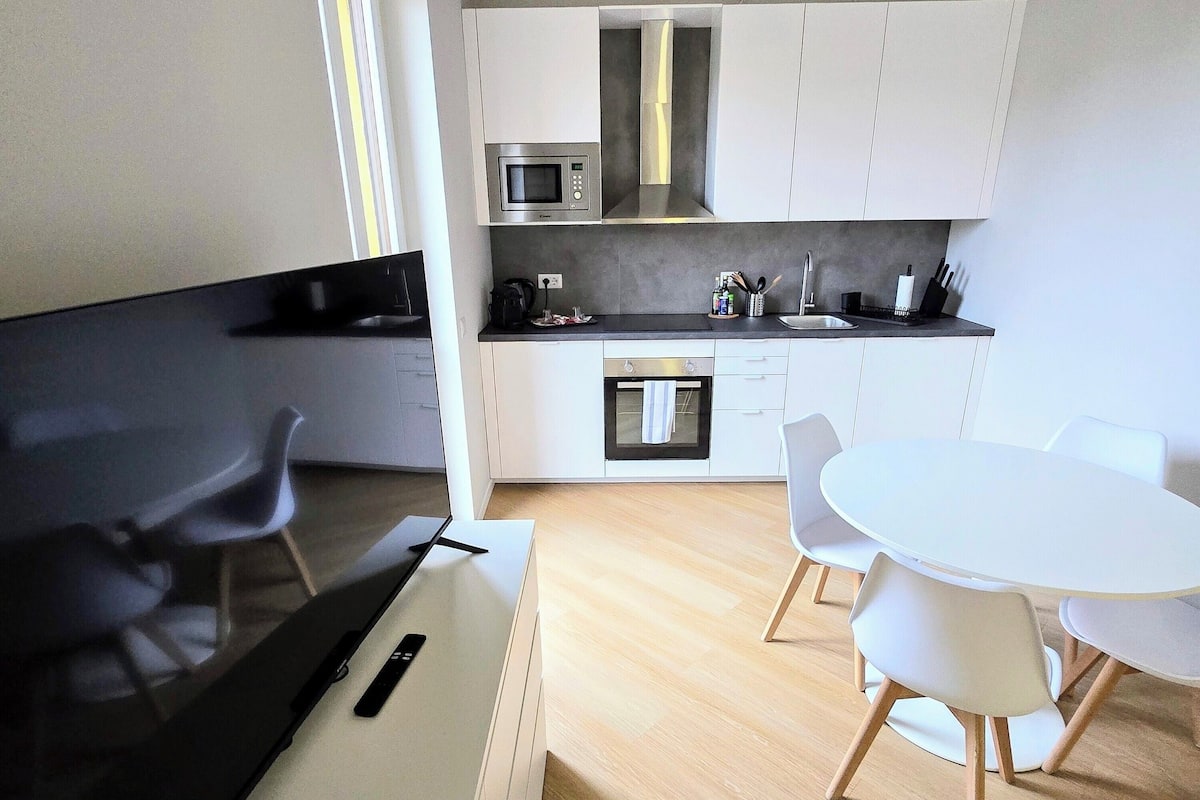 A modern kitchen with white cabinets, a microwave, and a stove. There is a dining area with a white table and chairs.