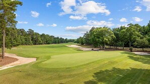 A golf course with a clear sky, green grass, sand bunkers, and trees. - Spacious 3BR True Blue Condo | Pool Access • Close to Golf & Beach (Pawleys Island)