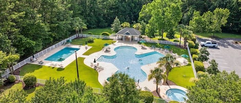 A large outdoor swimming pool area with multiple pools and lounge chairs, surrounded by well-maintained lawns and trees.