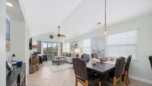 A spacious living area with a dining table, chairs, and a ceiling fan. - Spacious 3BR True Blue Condo | Pool Access • Close to Golf & Beach (Pawleys Island)