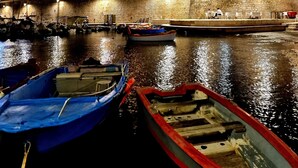 Un bâtiment historique en pierre, entouré de douves, avec des bateaux amarrés devant et une petite scène agrémentée de tables et de chaises.