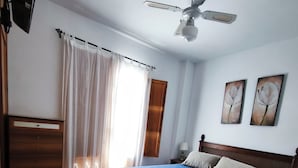 A bedroom with a bed, a desk, a ceiling fan, and two wall-mounted paintings. - El Mirador del Berenjenal. 
¡Relajate con toda la familia!.  (Enix)