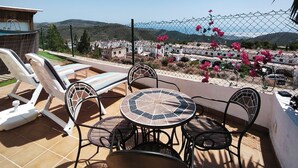 A patio with a table and chairs, a pool, and a view of a residential area with hills and pink flowers. - El Mirador del Berenjenal. 
¡Relajate con toda la familia!.  (Enix)
