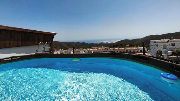 A swimming pool with clear blue water, surrounded by buildings and a view of a hilly landscape. - El Mirador del Berenjenal. 
¡Relajate con toda la familia!.  (Enix)