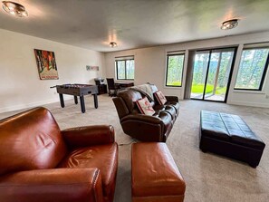 A living room with a brown leather sofa, a black leather ottoman, a brown leather armchair, a brown leather couch, a pool table, and a painting on the wall.