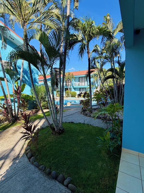 A pool area with a clear view of the pool, surrounded by palm trees and a building with a red roof.