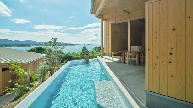 Une piscine avec vue sur la mer, une terrasse en bois et un espace salon couvert.