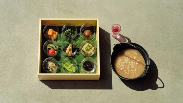 A wooden box containing nine small glass dishes with various food items, and a black bowl with a liquid beside it.
