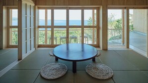 Une pièce avec des tatamis, une table ronde et de grandes fenêtres donnant sur la mer.