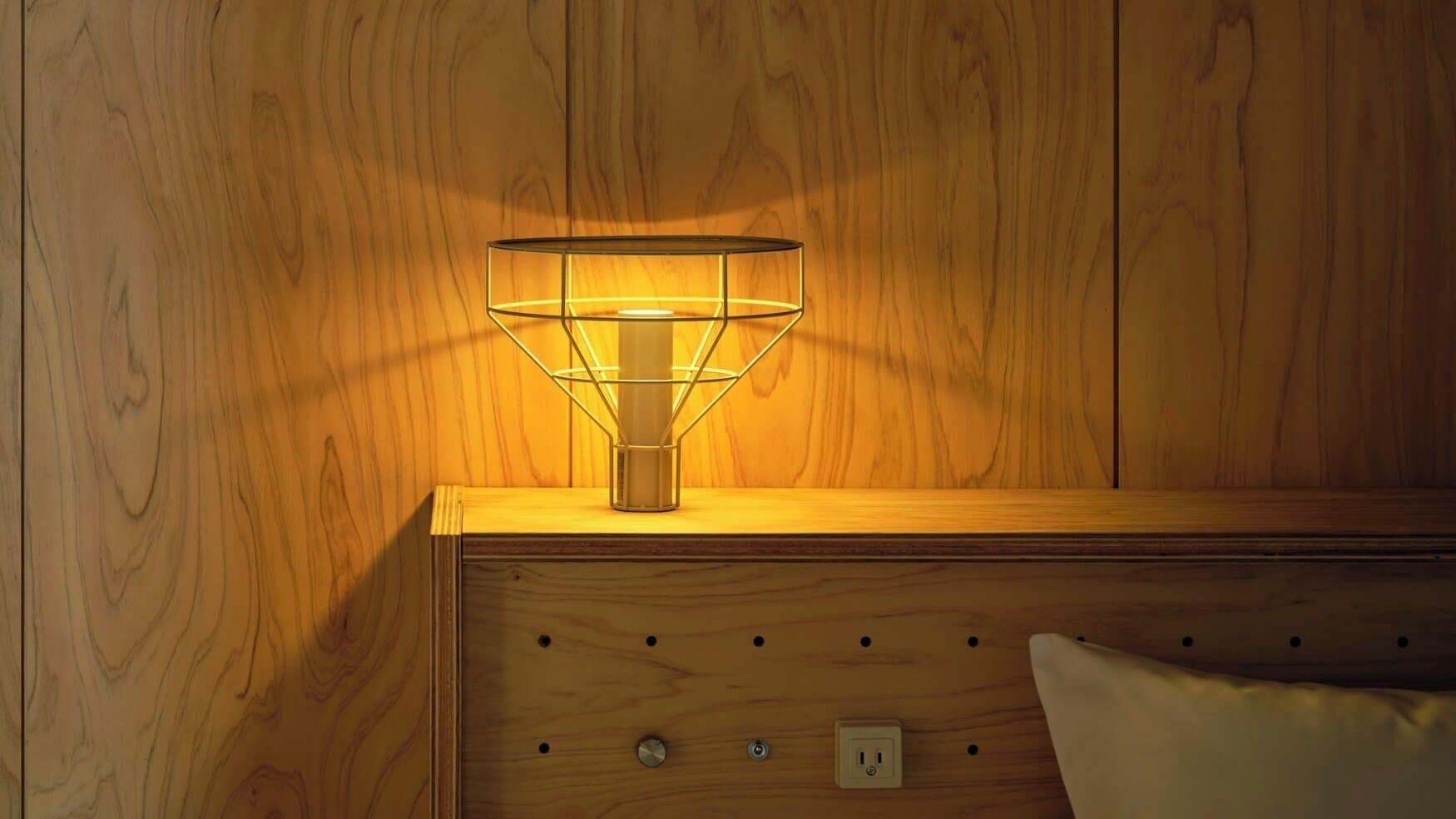 A wooden bedside table with a lamp, a power outlet, and a buttoned panel.