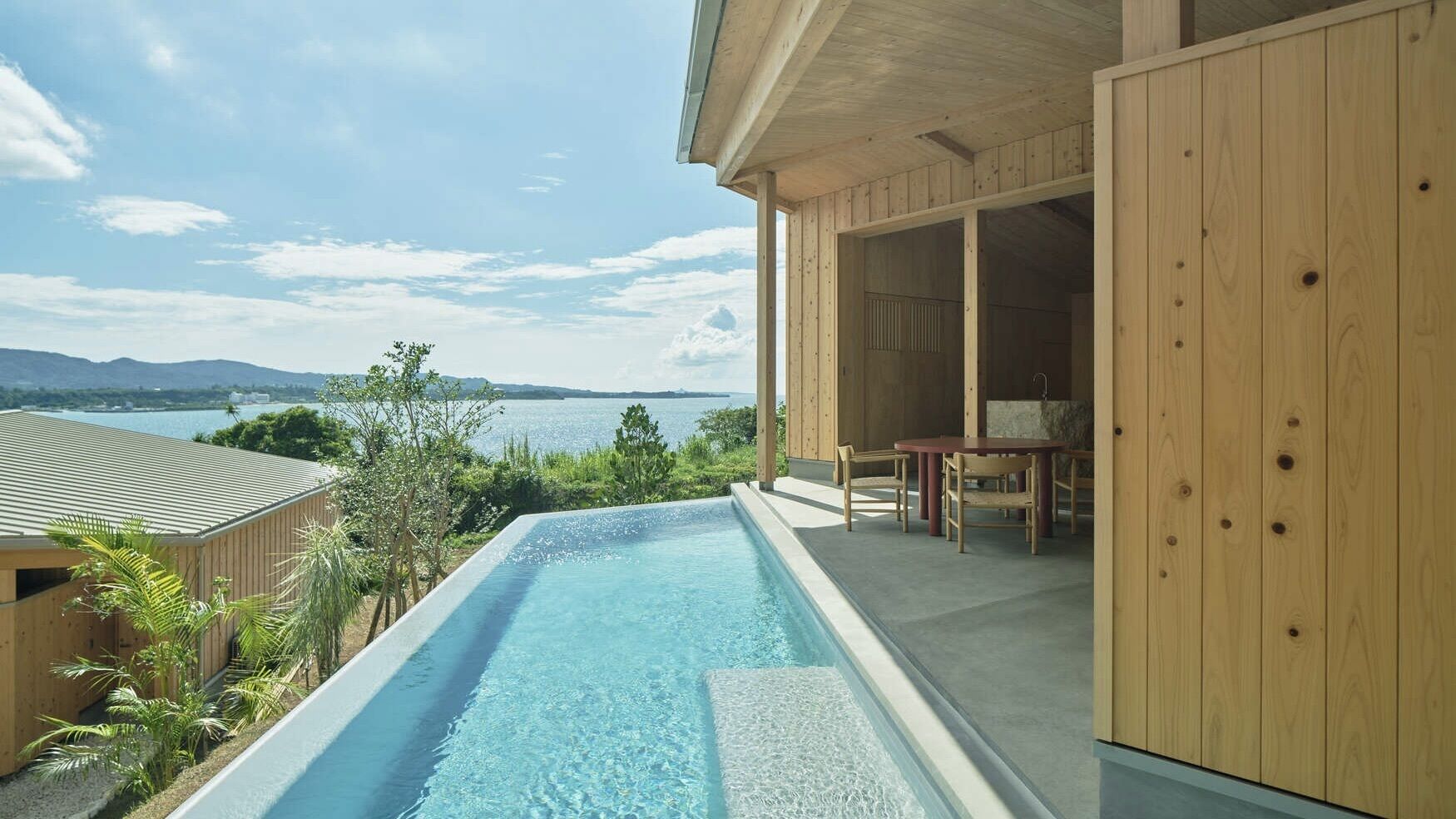 Ein Schwimmbecken mit Blick auf das Meer und die Berge, einer Holzterrasse und einem überdachten Sitzbereich.