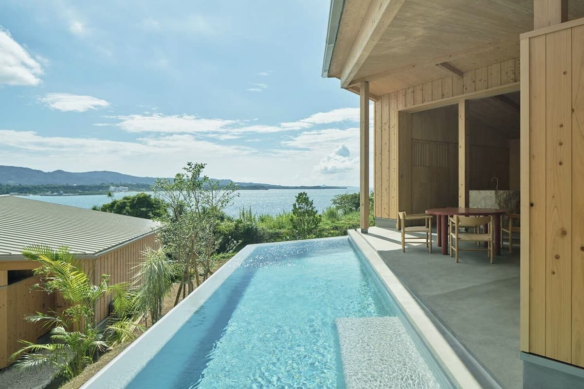 Piscina con vista al mar y montañas, terraza de madera y zona de estar cubierta.