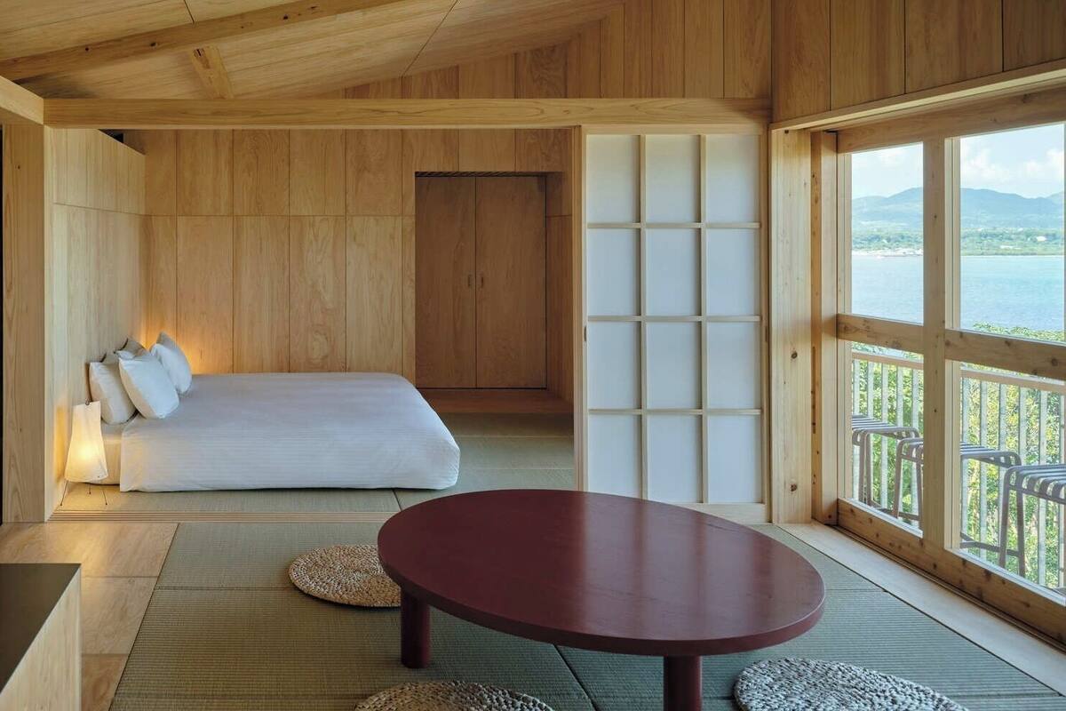 Een kamer met een bed, een ronde tafel en uitzicht op een wateroppervlak door grote ramen.