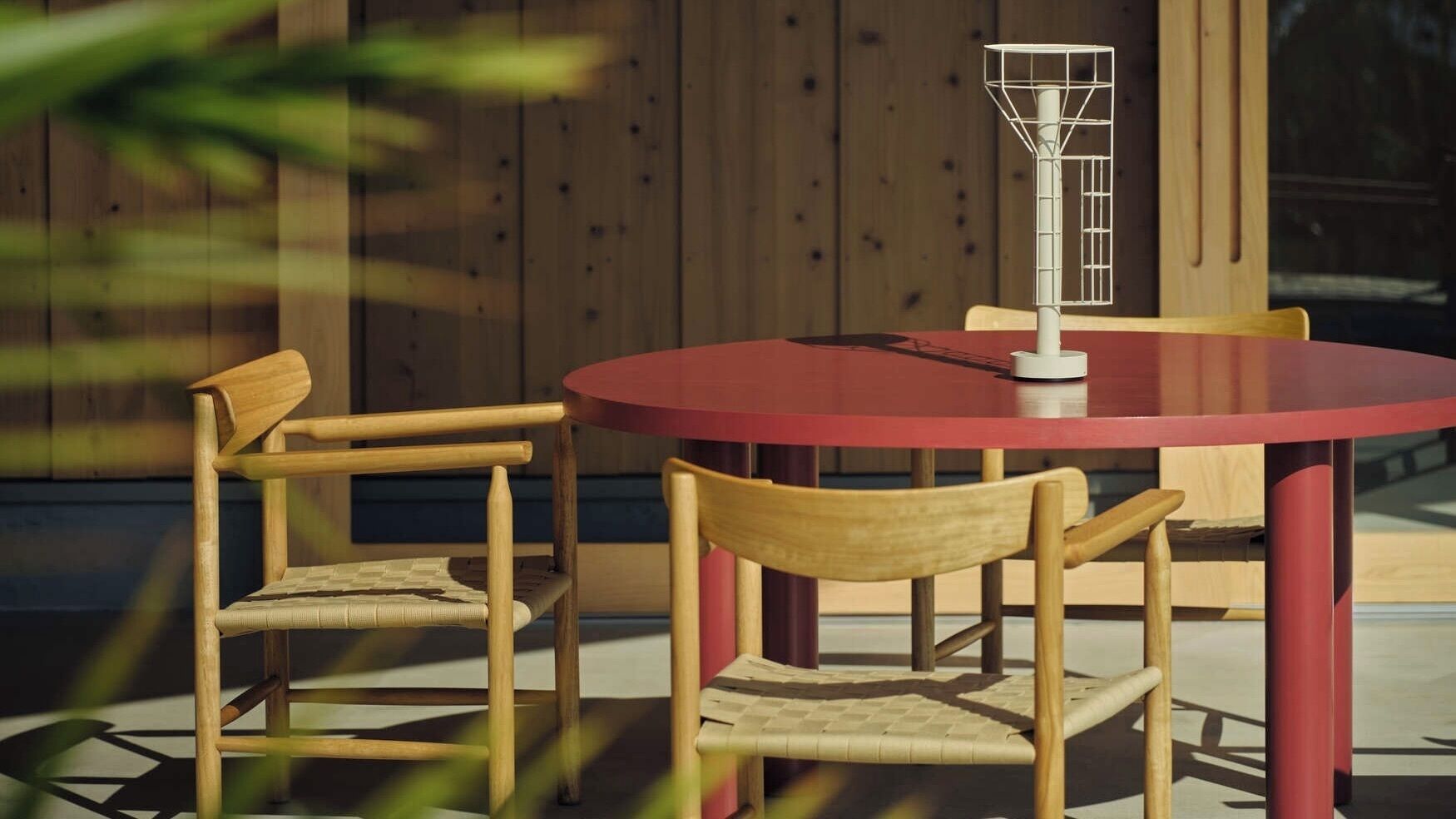 A round table with two wooden chairs, a red tablecloth, and a white object on the table.