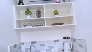 A compact kitchen with white cabinets, a built-in sink, a coffee maker, and a compact refrigerator. - Mactan Hostel (Lapu-Lapu)