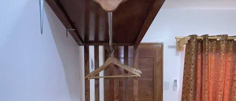 A small, compact room with a wooden table, a hanging coat rack, a bed with a yellow and black striped bedspread, and a door with a green lock.