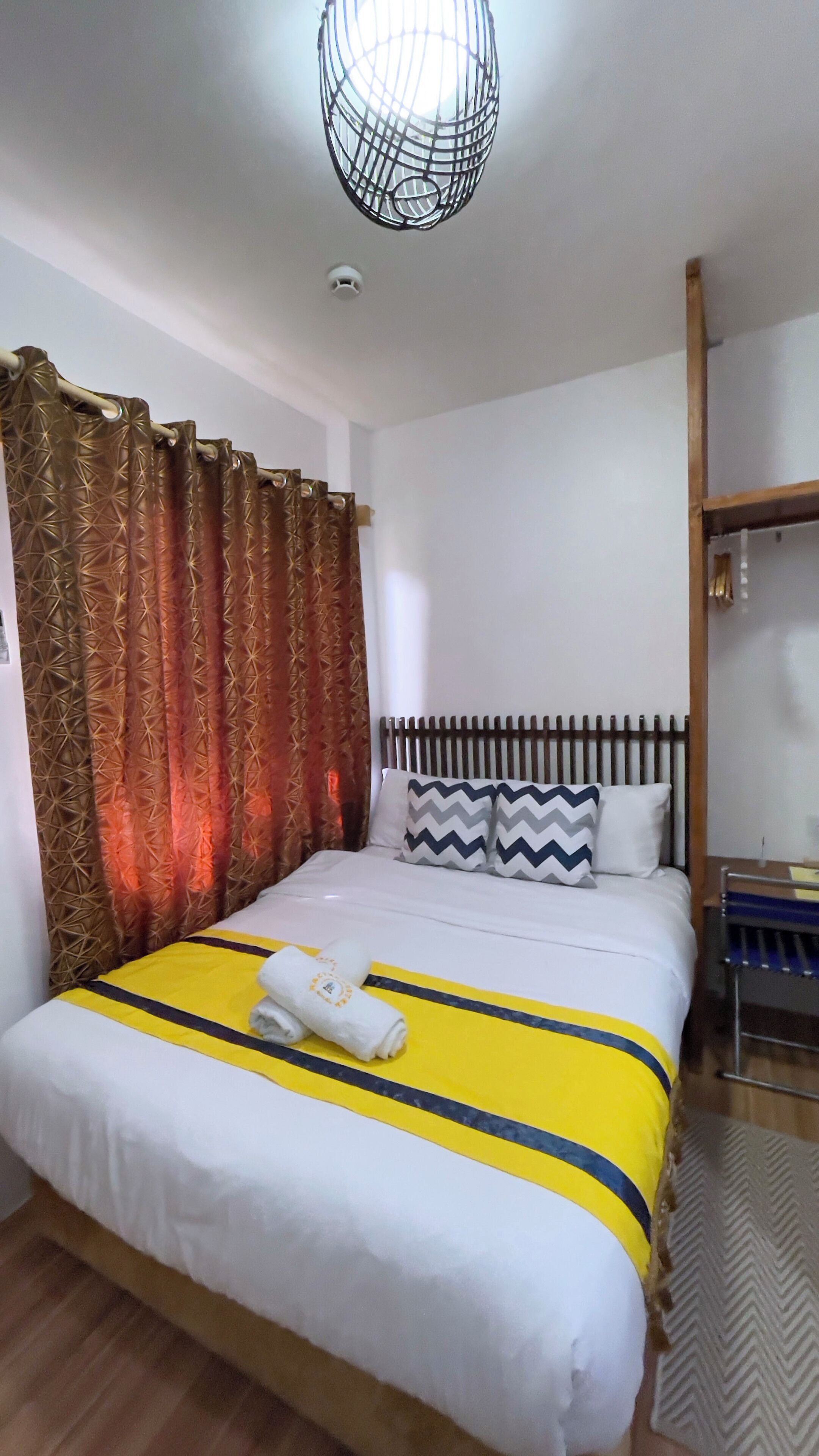 Una cama bien tendida con colcha a rayas amarilla y azul, una almohada blanca y una toalla enrollada.