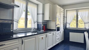 A kitchen with white cabinets, a black countertop, and a window with curtains. - El Rancho - 13801 (Güemes)