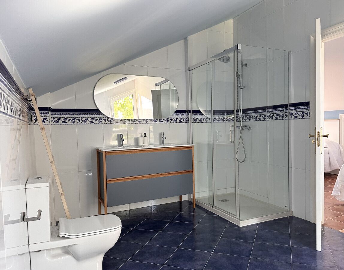 A modern bathroom with a glass shower enclosure, a wooden vanity, and a toilet.