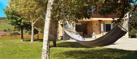 A hammock hanging between two trees in a grassy area with a building in the background.