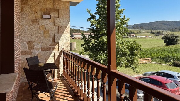 A balcony with stone walls, a wooden railing, and a view of a vineyard and hills. - El Rancho - 13801 (Güemes)