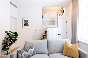 A modern living room with a grey sofa, a potted plant, and a framed artwork.