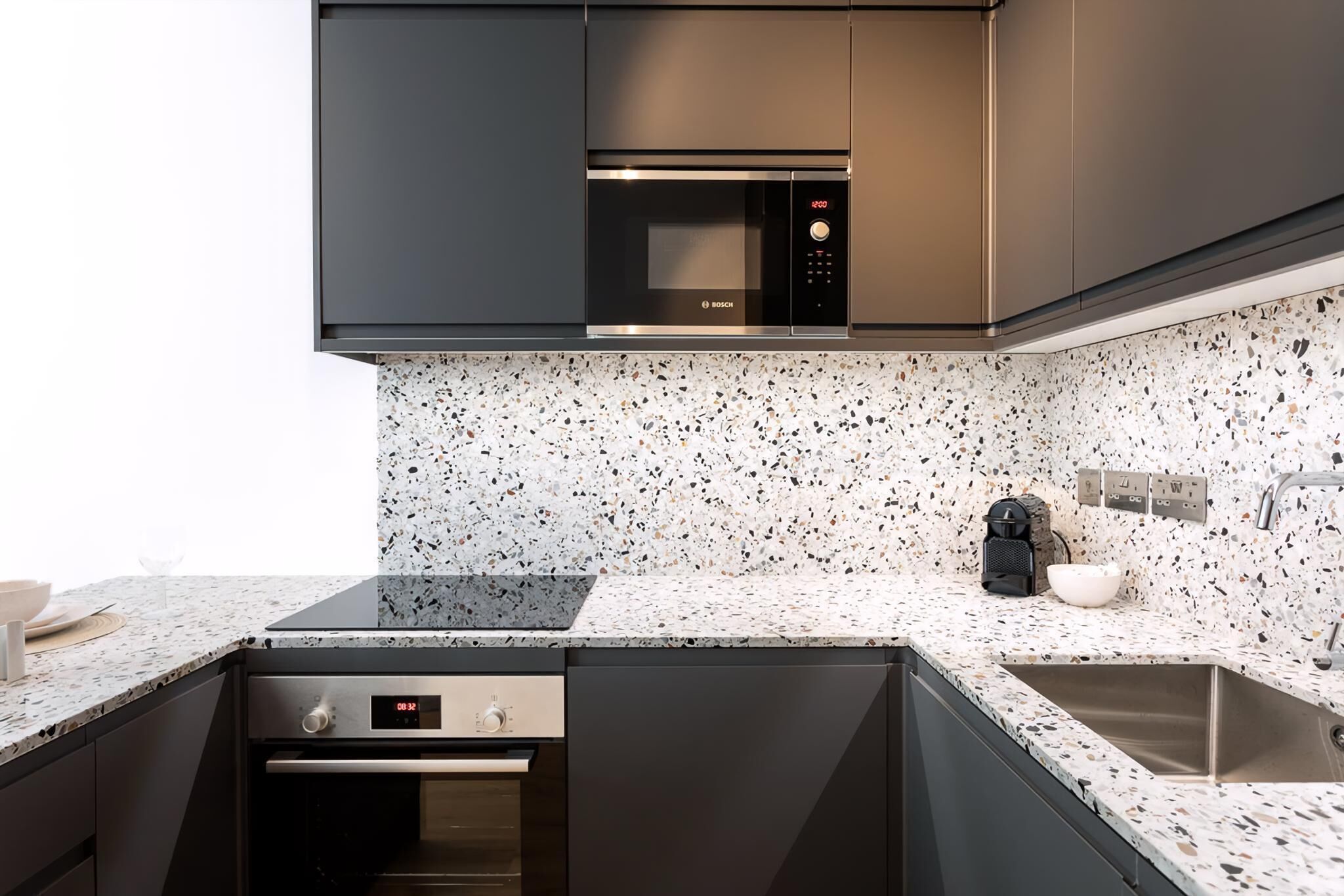 Uma cozinha moderna com micro-ondas Bosch, forno embutido, pia e painel de fundo com manchas.