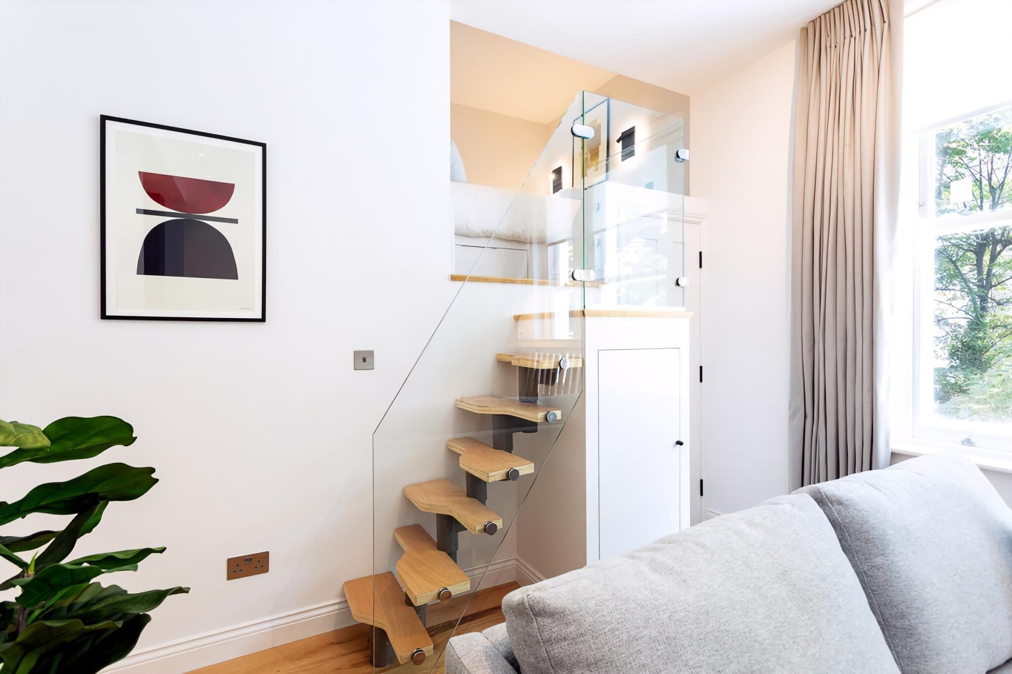 Een moderne trap met glazen balustrades en houten treden, een gekaderd kunstwerk aan de muur, en uitzicht op het omliggende landschap door een raam.