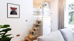 Un escalier moderne avec des rampes en verre et des marches en bois, une œuvre d’art encadrée au mur et une vue sur l’extérieur par une fenêtre.