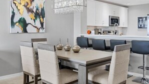 A modern dining area with a rectangular table, cushioned chairs, and a hanging crystal chandelier.