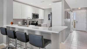 A modern kitchen with white cabinets, a central island with bar stools, a microwave, and a refrigerator.