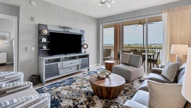 A modern living room with a flat-screen TV, a grey sofa, a coffee table, and a balcony with a view.