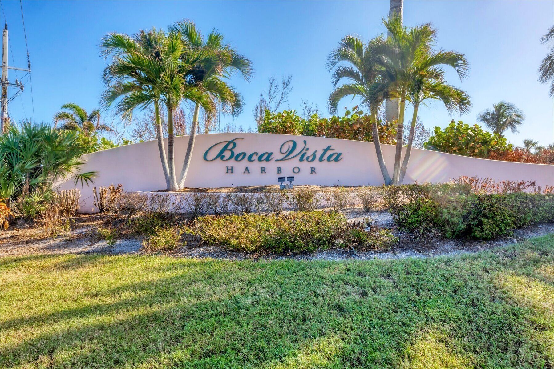 A sign for Boca Vista Harbor with palm trees and a grassy area in the foreground.