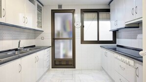 A modern kitchen with white cabinets, a stainless steel sink, and a window with blinds. - Comeback La Casa Sin Nombre (Motril)