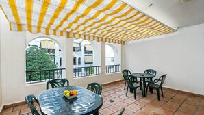 A covered outdoor patio with a tiled floor, green chairs, and a table with fruit. - Comeback La Casa Sin Nombre (Motril)