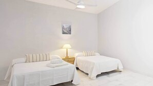 A hotel room with two beds, a nightstand with a lamp, and a ceiling fan. - Comeback La Casa Sin Nombre (Motril)